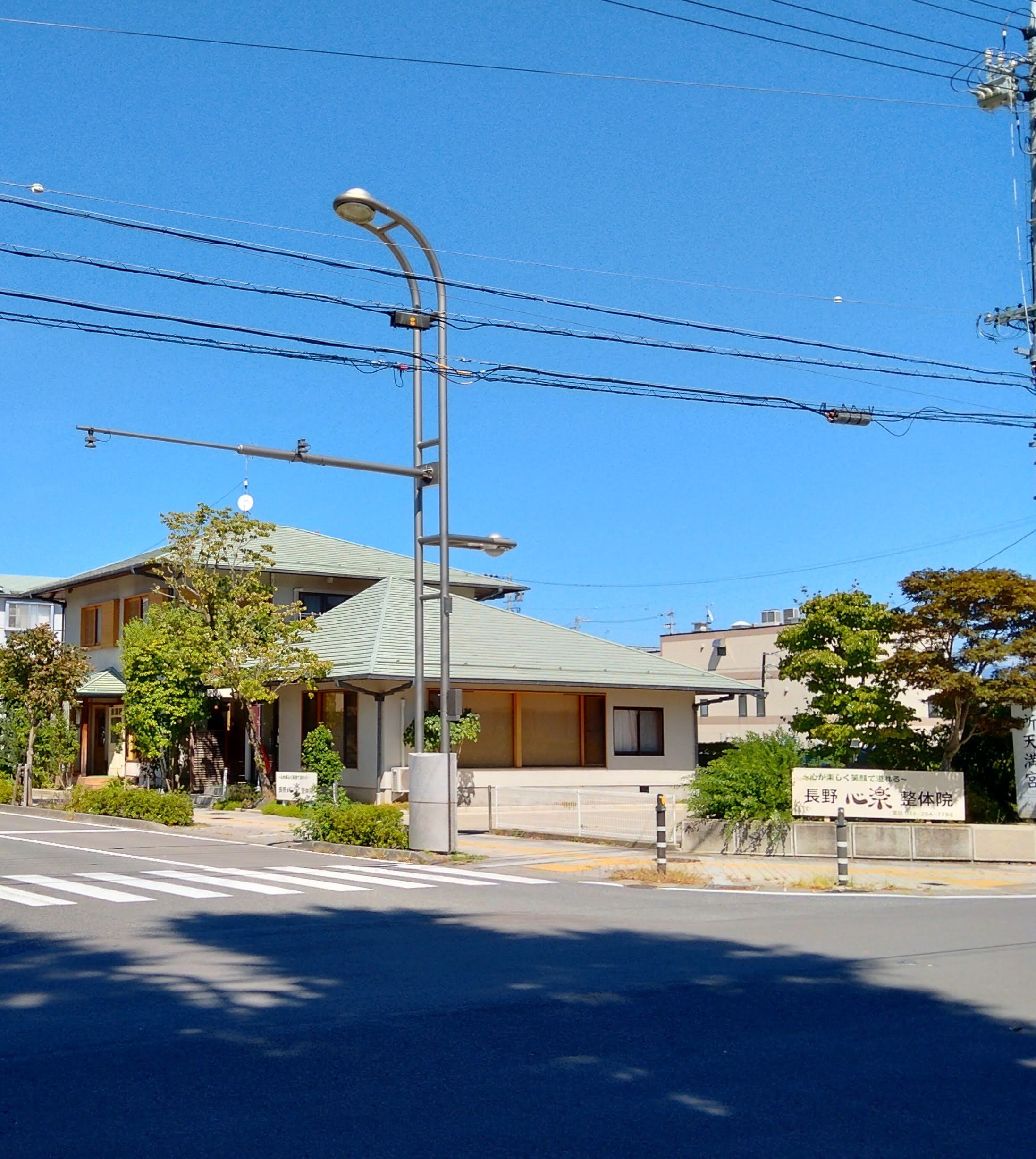 青空の下に見える長野心楽整体院の外観と看板