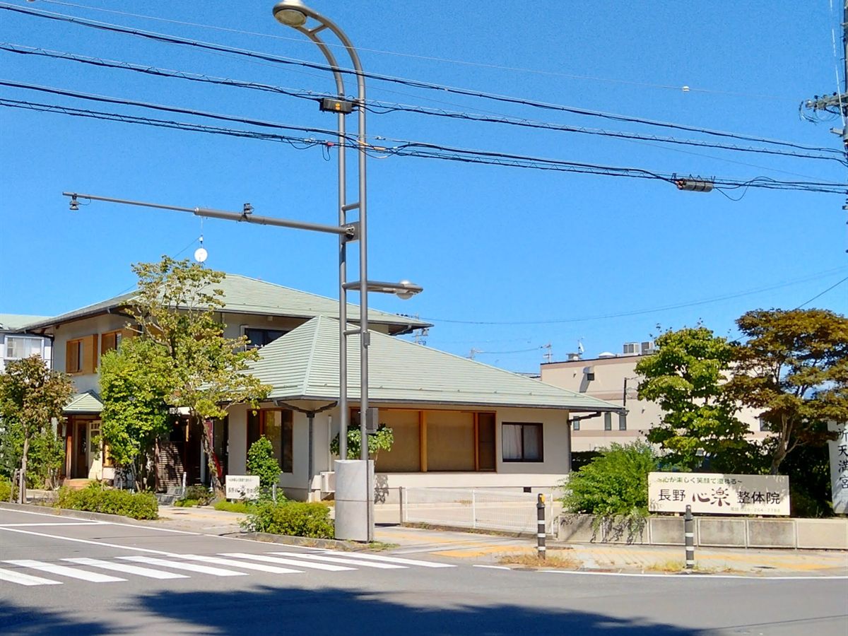 青空の下に見える長野心楽整体院の外観と看板